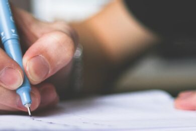 Close-up of hand writing in notebook using a blue pen, focus on creativity.