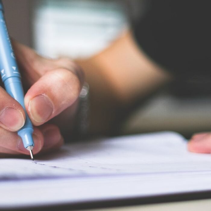 Close-up of hand writing in notebook using a blue pen, focus on creativity.