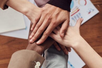 Diverse professionals unite for teamwork around a wooden table with laptops and documents.