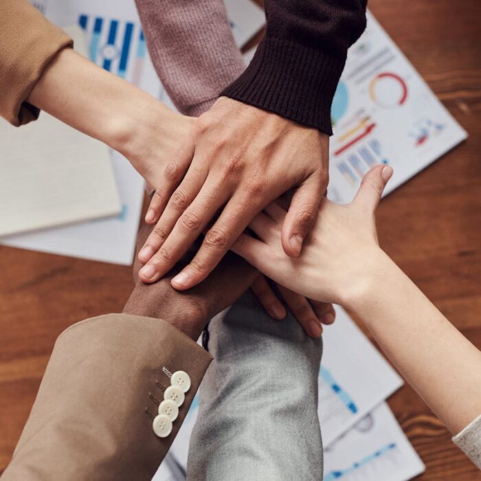 Diverse professionals unite for teamwork around a wooden table with laptops and documents.
